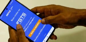 A imagem mostra uma pessoa segurando um celular e na tela, o app do FGTS para representar a liberação do FGTS que o governo vai liberar.