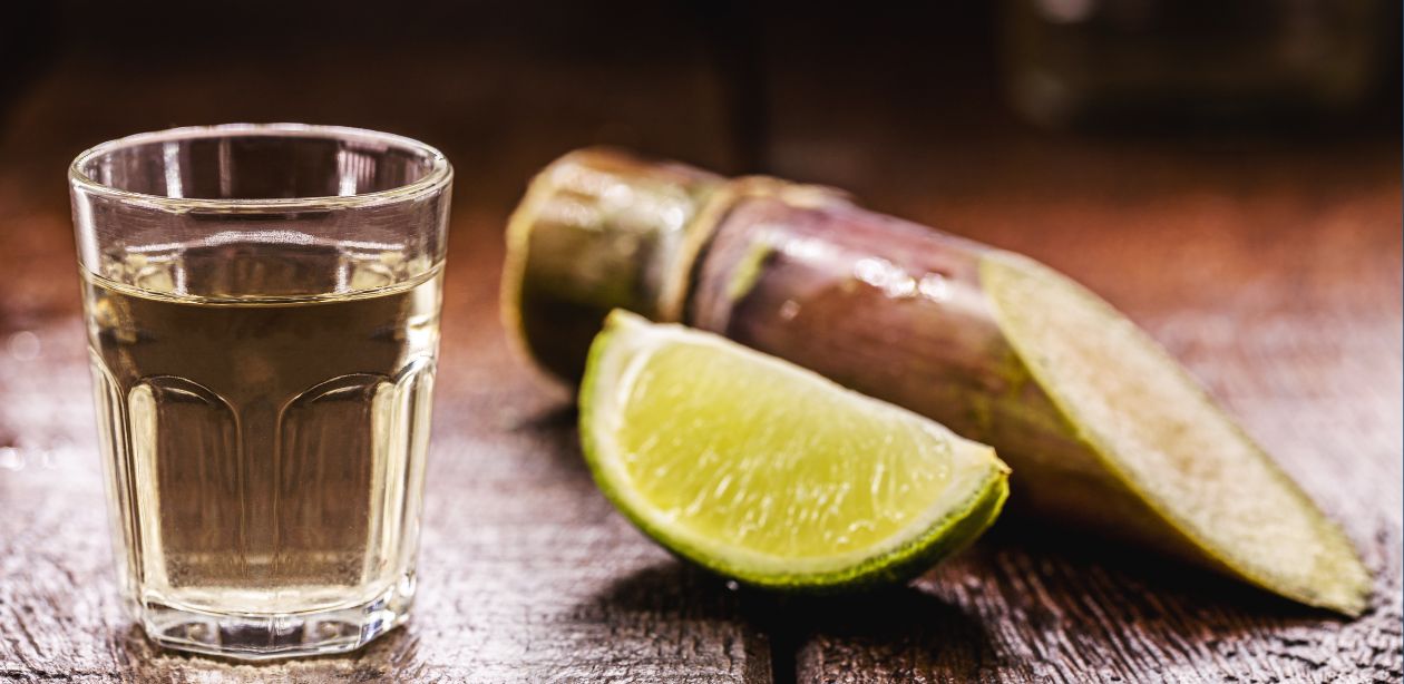 A imagem mostra um destilado, metade de um limão e um pedaço de cana, simbolizando o mercado de bebidas premium.