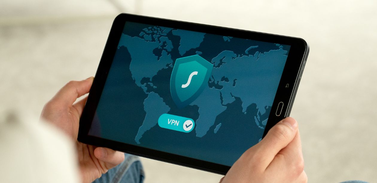 A imagem mostra uma pessoa segurando um tablet com a imagem de uma VPN conectada.