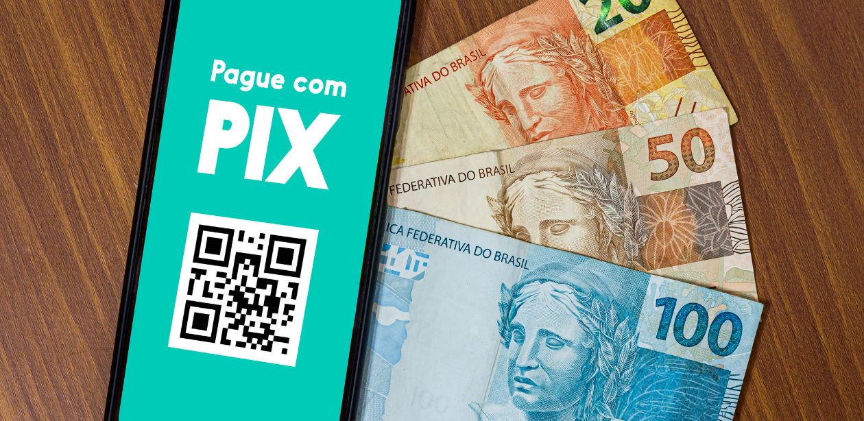 A imagem mostra um celular com um QR Code para pagamento via Pix e ao lado, notas de dinheiro, simbolizando a tecnologia do Pix na economia.