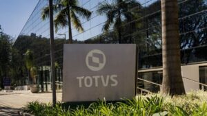 Fachada da sede da Totvs com logo da empresa em destaque, cercada por vegetação e refletindo a modernidade do prédio envidraçado.