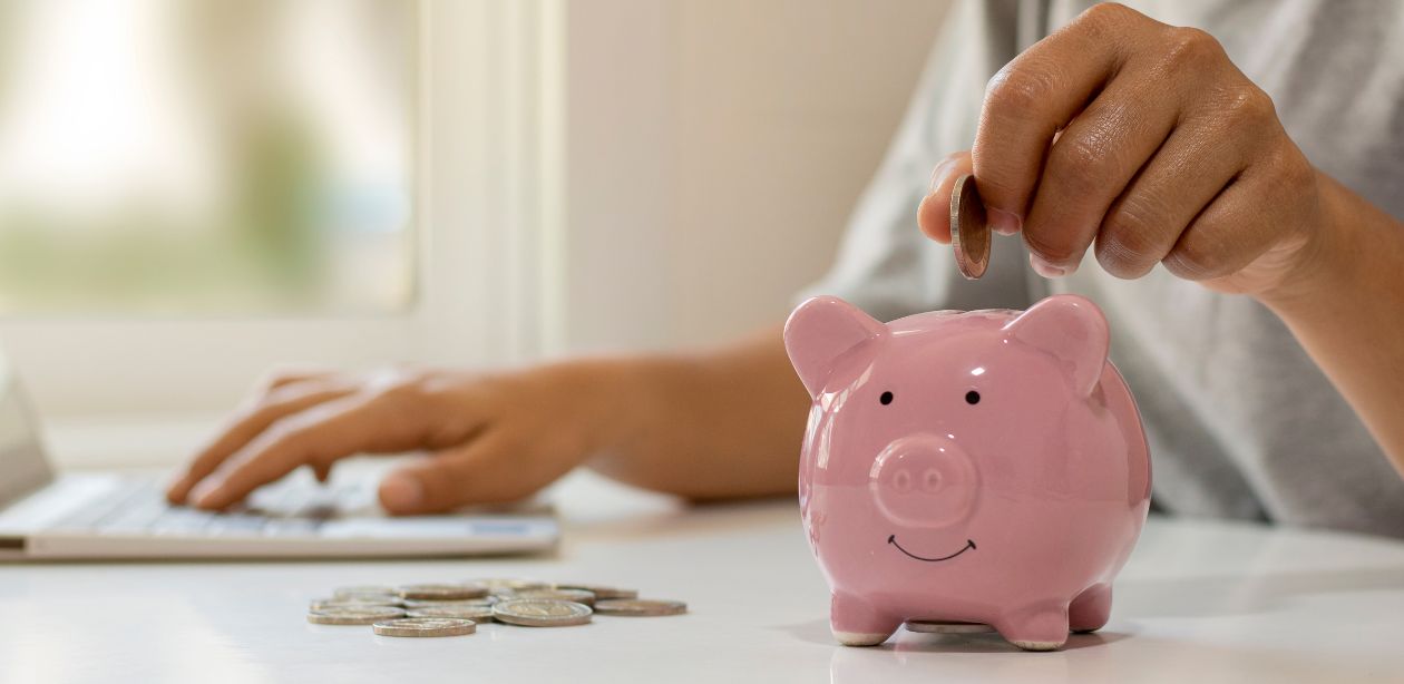 A imagem mostra uma pessoa colocando dinheiro em um cofre de porquinho e várias moedas em cima da mesa, representando os setores para investir e lucrar mais.