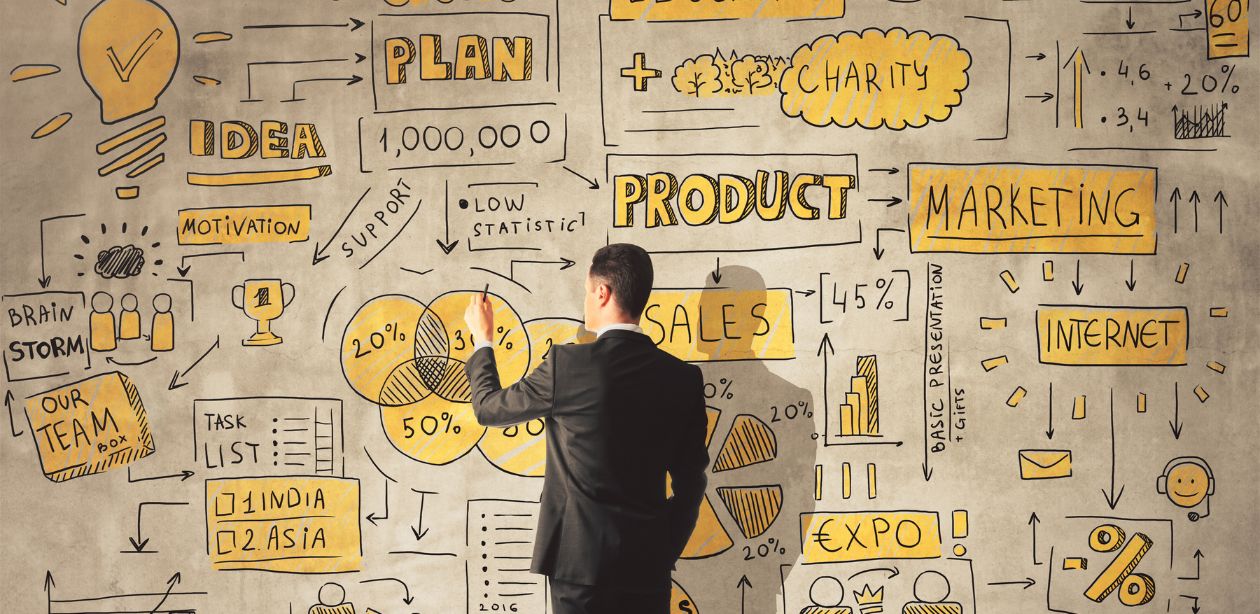 Homem de terno escreve em um grande painel com gráficos, diagramas e palavras-chave sobre negócios e planejamento, ilustrando estratégias empresariais e financeiras em um contexto de possíveis impactos do task masking.