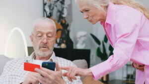 Casal idoso analisando informações financeiras em um smartphone, destacando o Tesouro Renda+ Aposentadoria Extra como alternativa de investimento seguro.