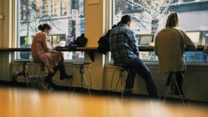 Pessoas trabalhando remotamente em um café, utilizando notebooks, refletindo a flexibilidade e os impactos do trabalho remoto na economia.