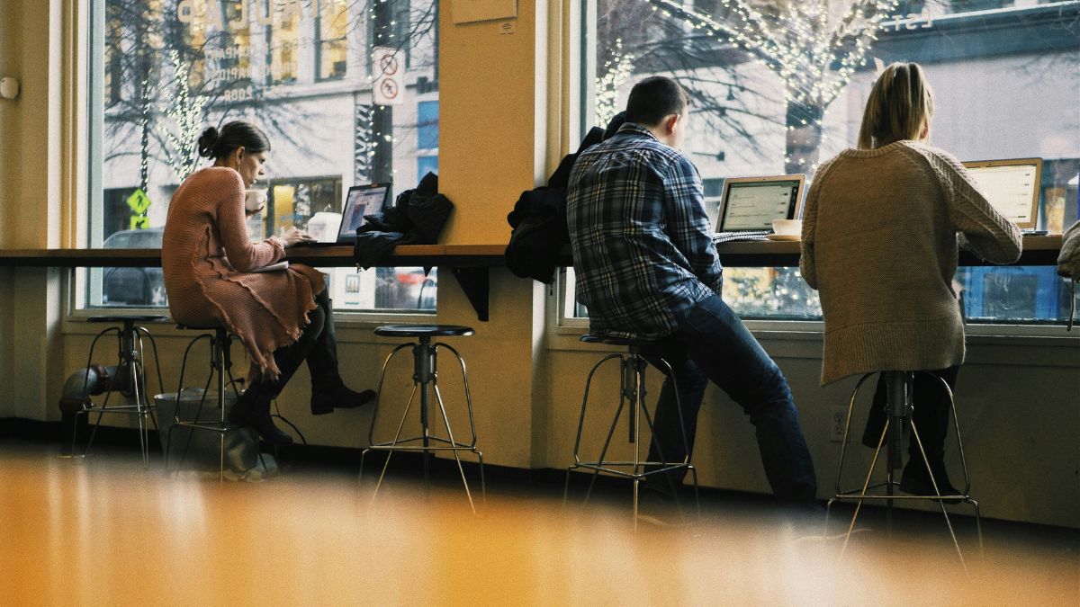 Pessoas trabalhando remotamente em um café, utilizando notebooks, refletindo a flexibilidade e os impactos do trabalho remoto na economia.