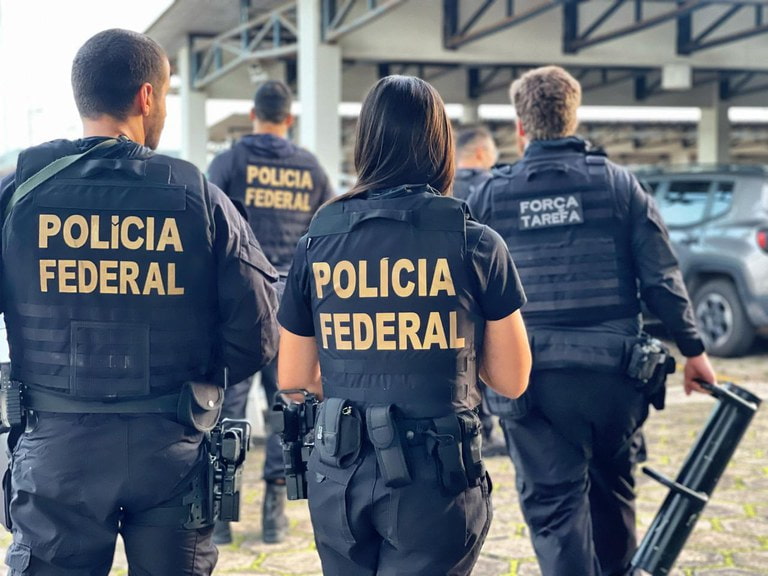 Agentes da Polícia Federal e da Força-Tarefa durante operação investigando lavagem de dinheiro em fintechs, caminhando em um estacionamento