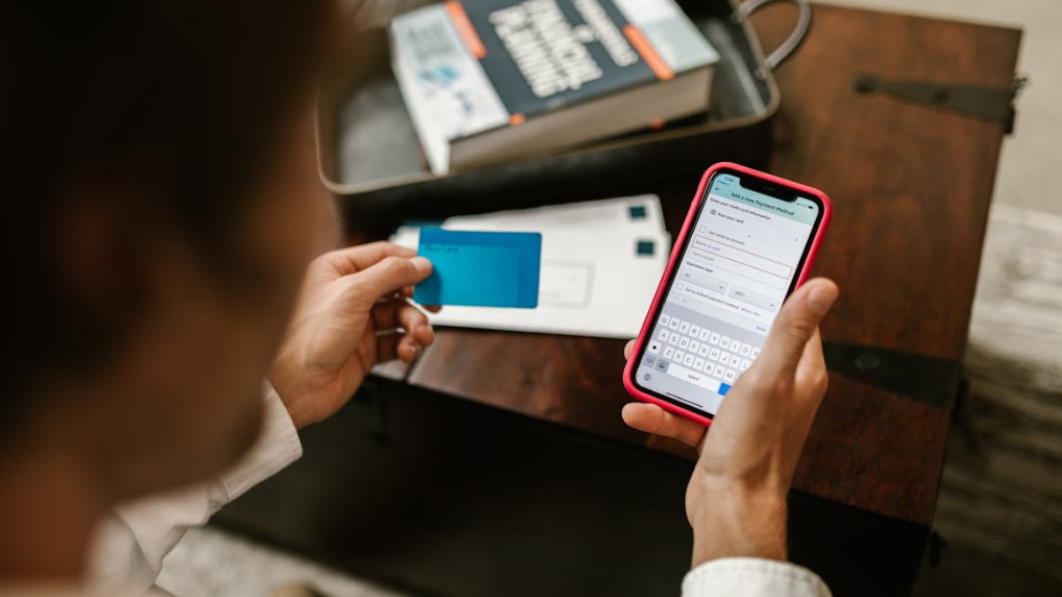 Pessoa segurando um cartão de crédito enquanto insere dados de pagamento em um smartphone. Representação de compras online e possíveis riscos de fraudes digitais.