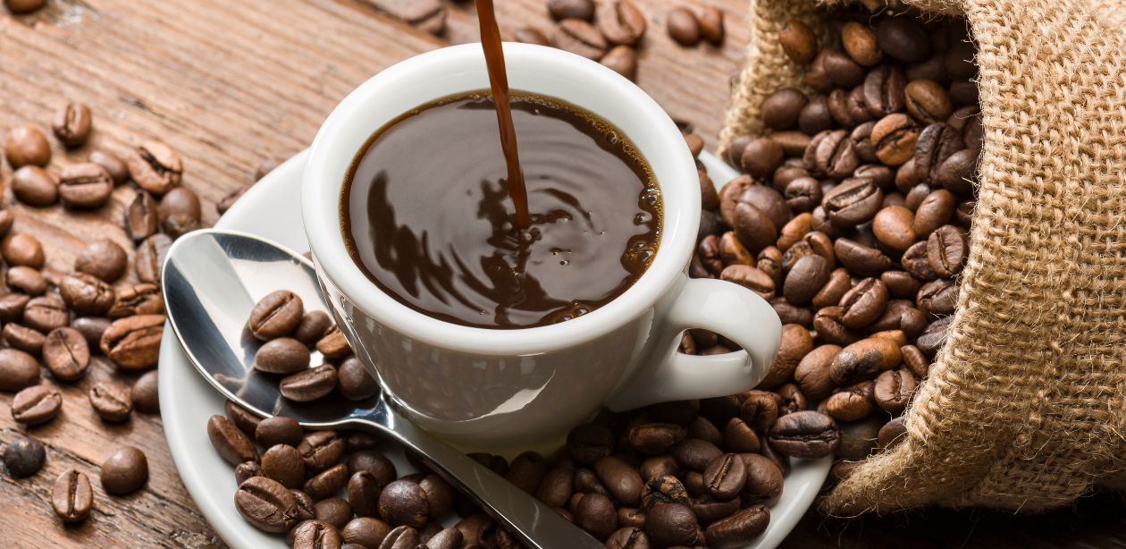 A imagem mostra uma xícara de café em meio a vários grãos de café para representar a alta do café.