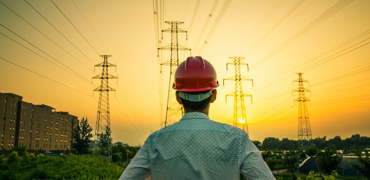 A imagem mostra um homem de costas olhando para várias torres de energia para representar a CPFL Energia.