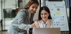A imagem mostra duas mulheres na frente de um notebook para representar o consultor financeiro.