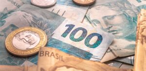 A imagem mostra cédulas de real e moedas para representar o déficit primário.