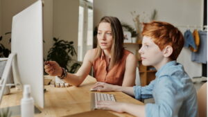 Mãe ensinando filho no computador, representando dicas de educação financeira para crianças e a importância do aprendizado sobre dinheiro desde cedo.