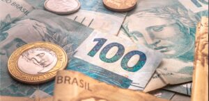 A imagem mostra várias notas de real e moedas para representar a dívida pública.