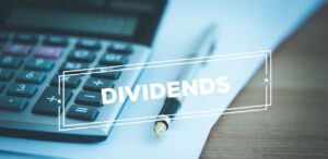 A imagem mostra ao fundo um papel, calculadora e caneta e na frente escrito dividends para representar os Dividendos do XPLG11.