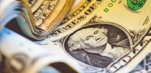 A imagem mostra várias notas de dólares para representar que o dólar cai a R$5,67.