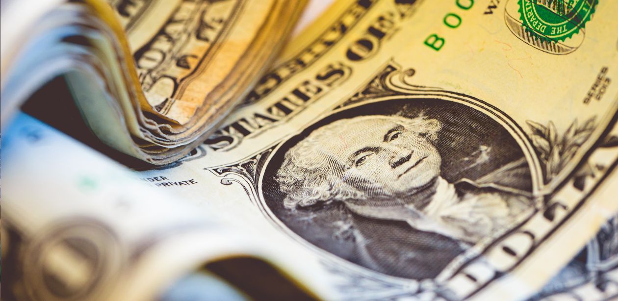 A imagem mostra várias notas de dólares para representar que o dólar cai a R$5,67.