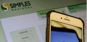 A imagem mostra a tela de um notebook no site do Simples Nacional e um celular para representar a emissão de notas fiscais por MEIs