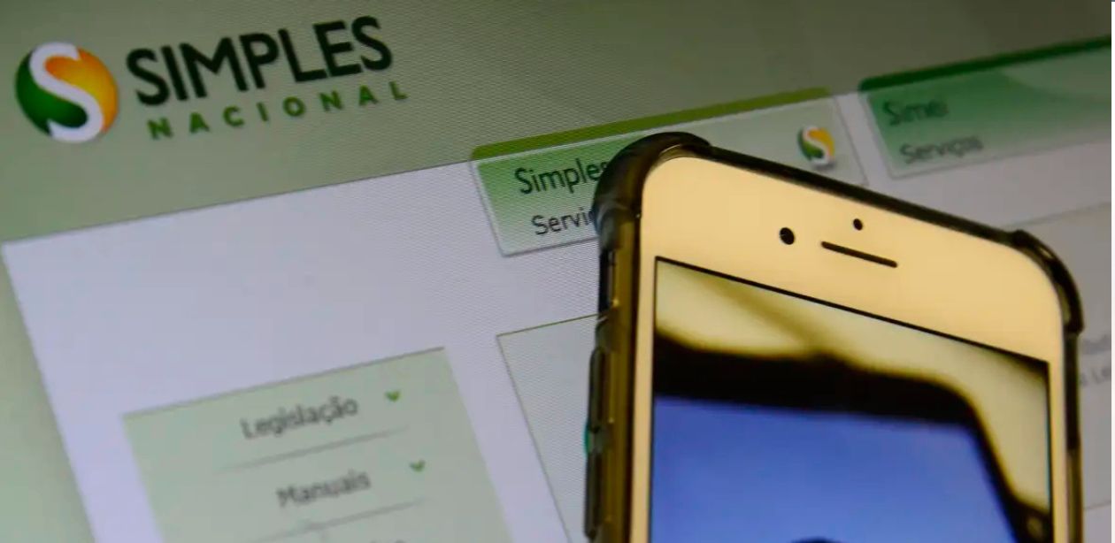 A imagem mostra a tela de um notebook no site do Simples Nacional e um celular para representar a emissão de notas fiscais por MEIs
