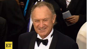 Gene Hackman sorrindo em um evento formal, vestindo smoking e gravata borboleta. Foto do tapete vermelho.
