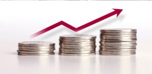 A imagem mostra uma seta subindo e várias moedas para representar a inflação ao consumidor.