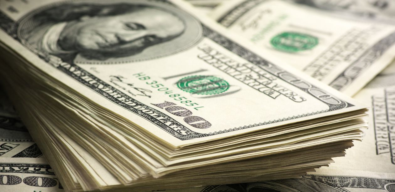 A imagem mostra várias notas de dólares para representar o mercado financeiro.