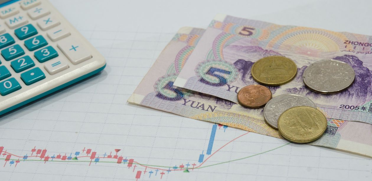 A imagem mostra um gráfico desenhado em um papel e moedas para representar o mercado financeiro.