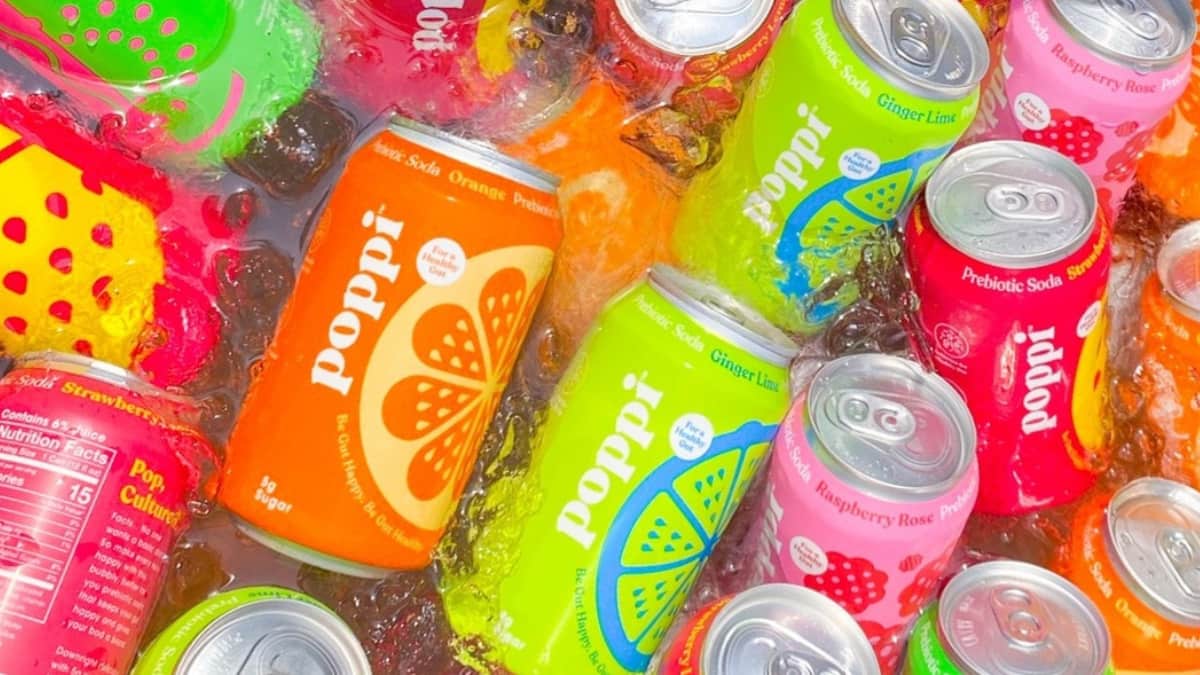 Latas de refrigerante prebiótico Poppi em diferentes sabores mergulhadas em gelo, destacando a recente aquisição da marca pela PepsiCo.