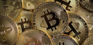 A imagem mostra diversas moedas de Bitcoin para representar a queda do Bitcoin.