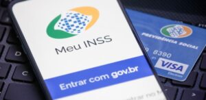 A imagem mostra um cartão de benefício INSS, um celular com o início do app Meu INSS para representar a revisão de benefícios.