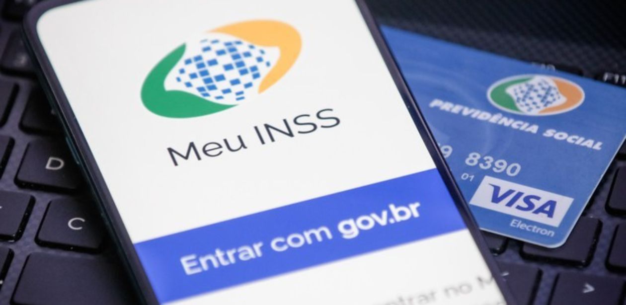 A imagem mostra um cartão de benefício INSS, um celular com o início do app Meu INSS para representar a revisão de benefícios.