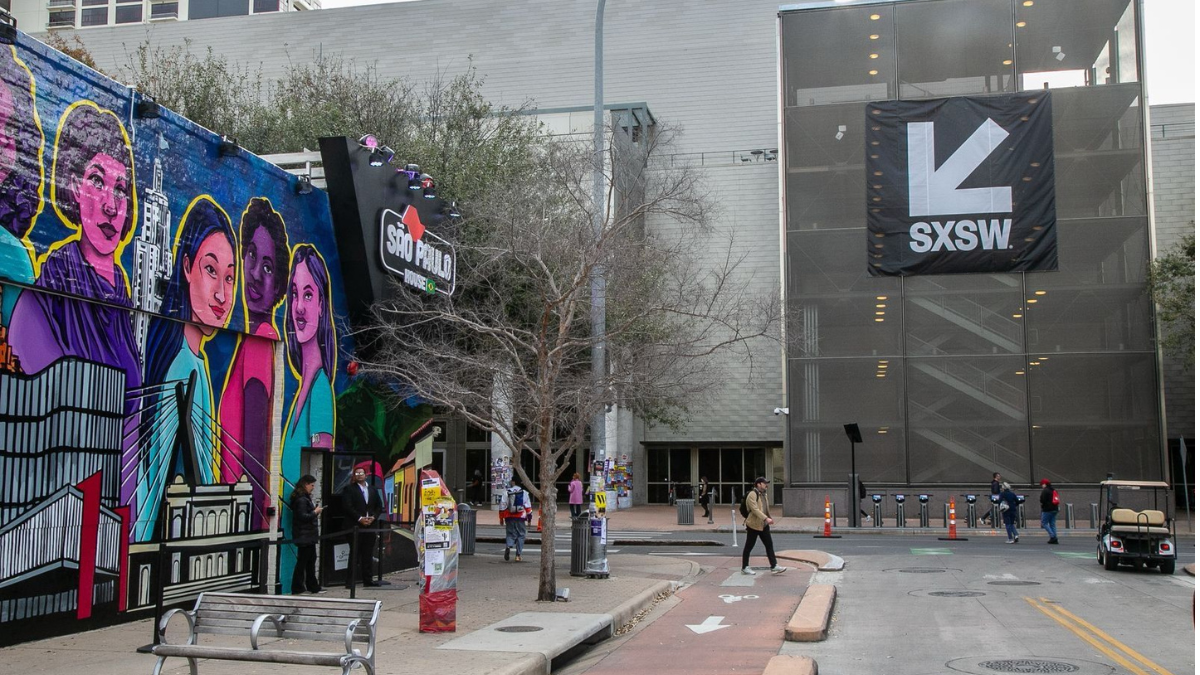 Fachada da SP House no SXSW, com mural artístico representando São Paulo e banner do evento South by Southwest em Austin, EUA.
