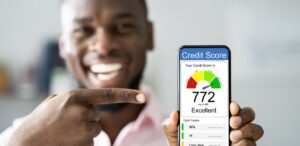 A imagem mostra um homem desfocado segurando um celular e na tela aparece um gráfico de score de crédito.