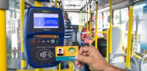 A imagem mostra uma pessoa dentro de um ônibus segurando um cartão de Bilhete Único.