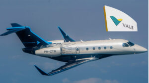 Jato executivo Praetor 500 da Embraer em voo, com a logo da Vale ao fundo, destacando a recente aquisição da empresa após prejuízo financeiro.