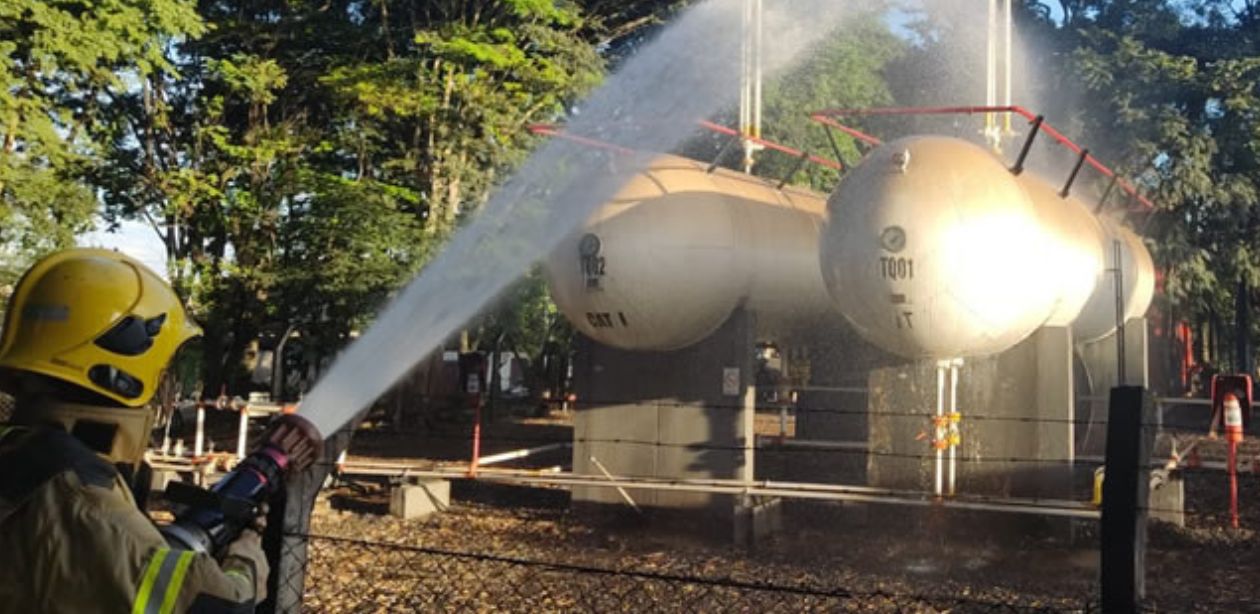 A imagem mostra um bombeiro jogando água nos tanques da Fermavi para conter o vazamento de gás GLP.
