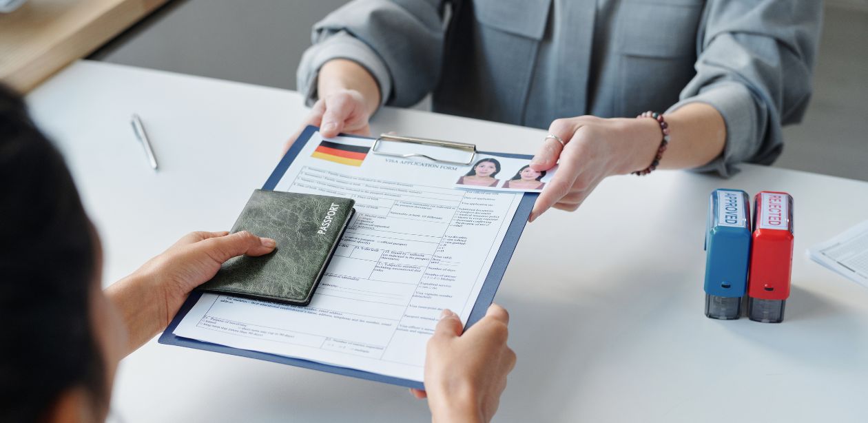 A imagem mostra uma pessoa entregando o visto e vários documentos para outra pessoa par representar que o visto para turistas no Brasil voltará a ser obrigatório.