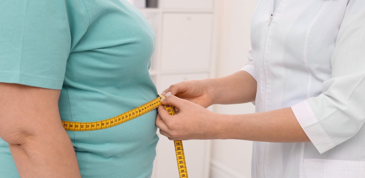 A imagem mostra uma pessoa medindo a barriga de uma pessoa obesa com uma fita métrica para representar a epidemia de sobrepeso.