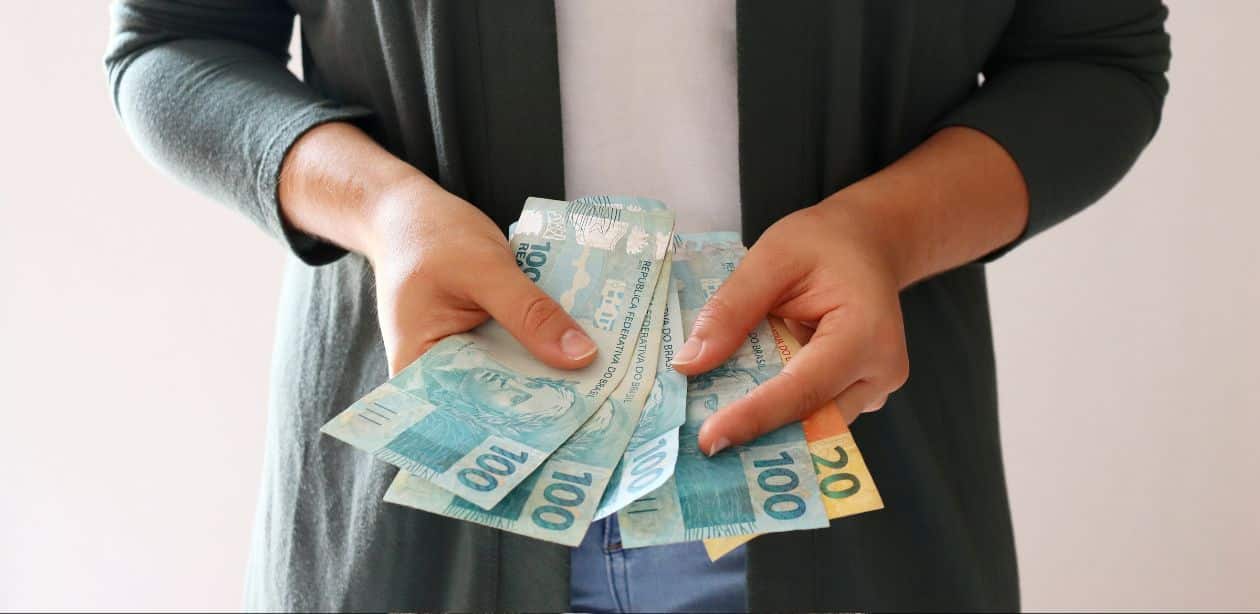 A imagem mostra uma pessoa segurando várias notas para representar o crédito consignado privado.
