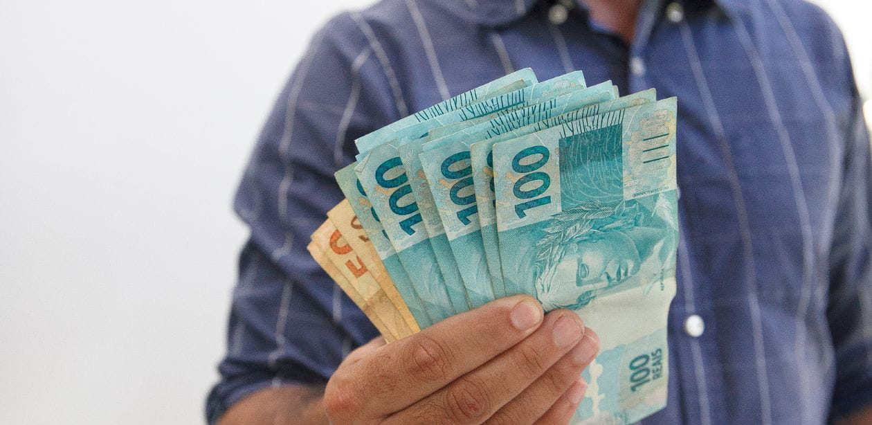 Mão segurando notas de reais representando empréstimo consignado CLT.