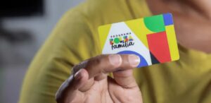 A imagem mostra uma pessoa segurando um cartão do Bolsa Família para representar a fiscalização de benefícios assistenciais.