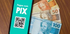 A imagem mostra um celular com um qr code e dinheiro para representar as fraudes no pix
