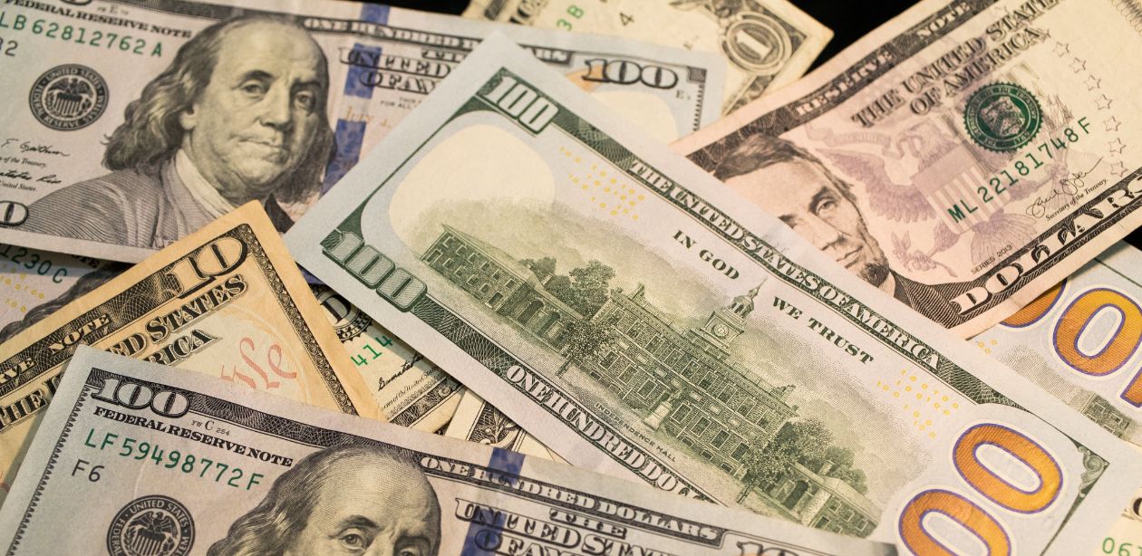 A imagem mostra várias notas de dólares para representar o mercado financeiro.