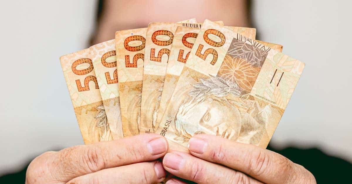 A imagem mostra uma pessoa segurando notas de real para representar o PIB do Brasil 2025