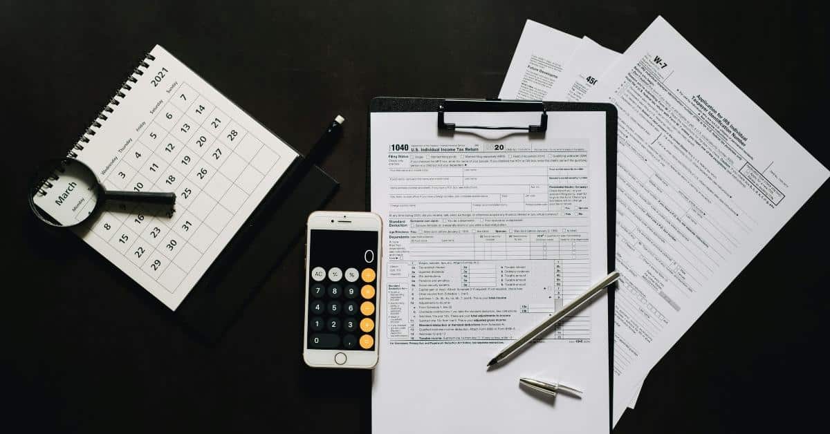 A imagem mostra vários papéis, calculadora e caneta sob uma mesa para representar a restituição do IRPF 2025