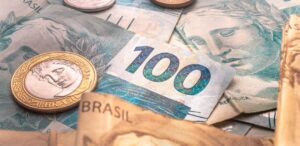 Cédulas e moedas do real desvalorizado frente ao dólar, com destaque para a nota de 100 reais.