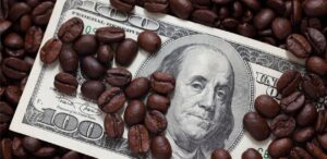 A imagem mostra grãos de café em volta de uma nota de dólar para representar o preço do café.