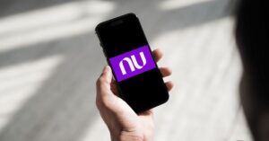 A imagem mostra uma pessoa segurando um celular com a logo da Nubank na tela para representar a Caixinha Turbo do Nubank