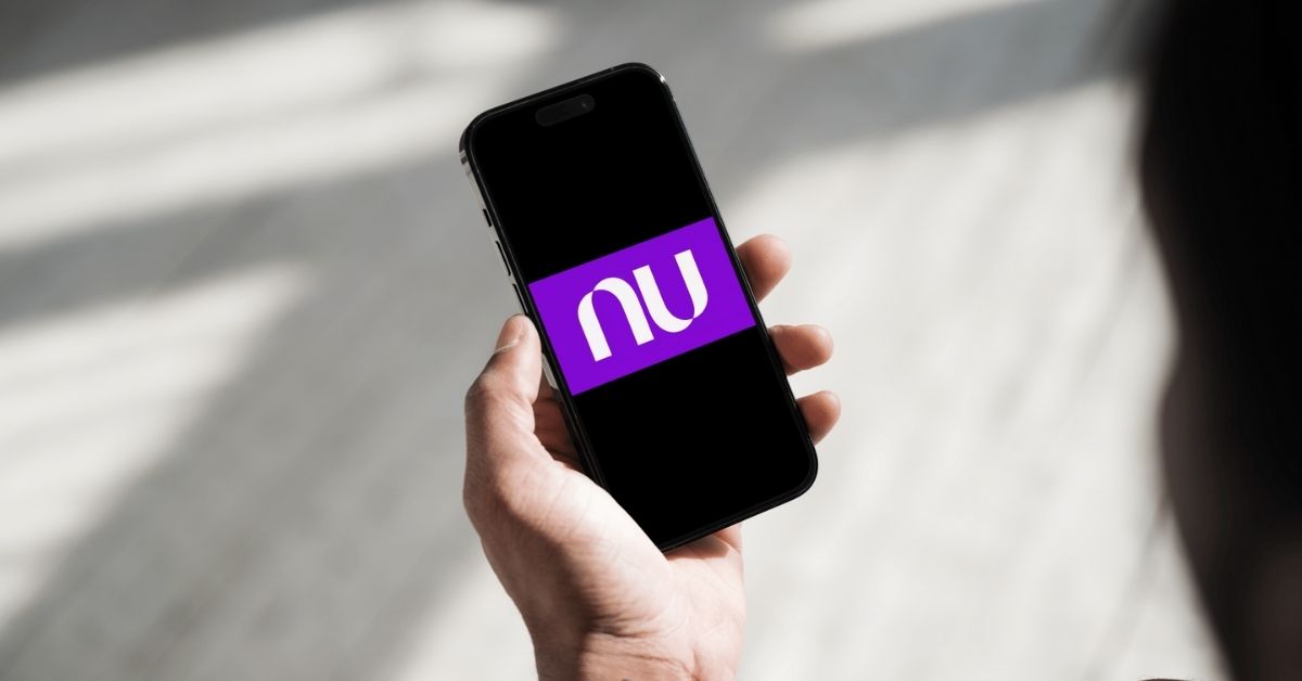A imagem mostra uma pessoa segurando um celular com a logo da Nubank na tela para representar a Caixinha Turbo do Nubank