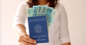 A imagem mostra uma mulher segurando uma carteira de trabalho e dinheiro para representar a portabilidade do consignado CLT